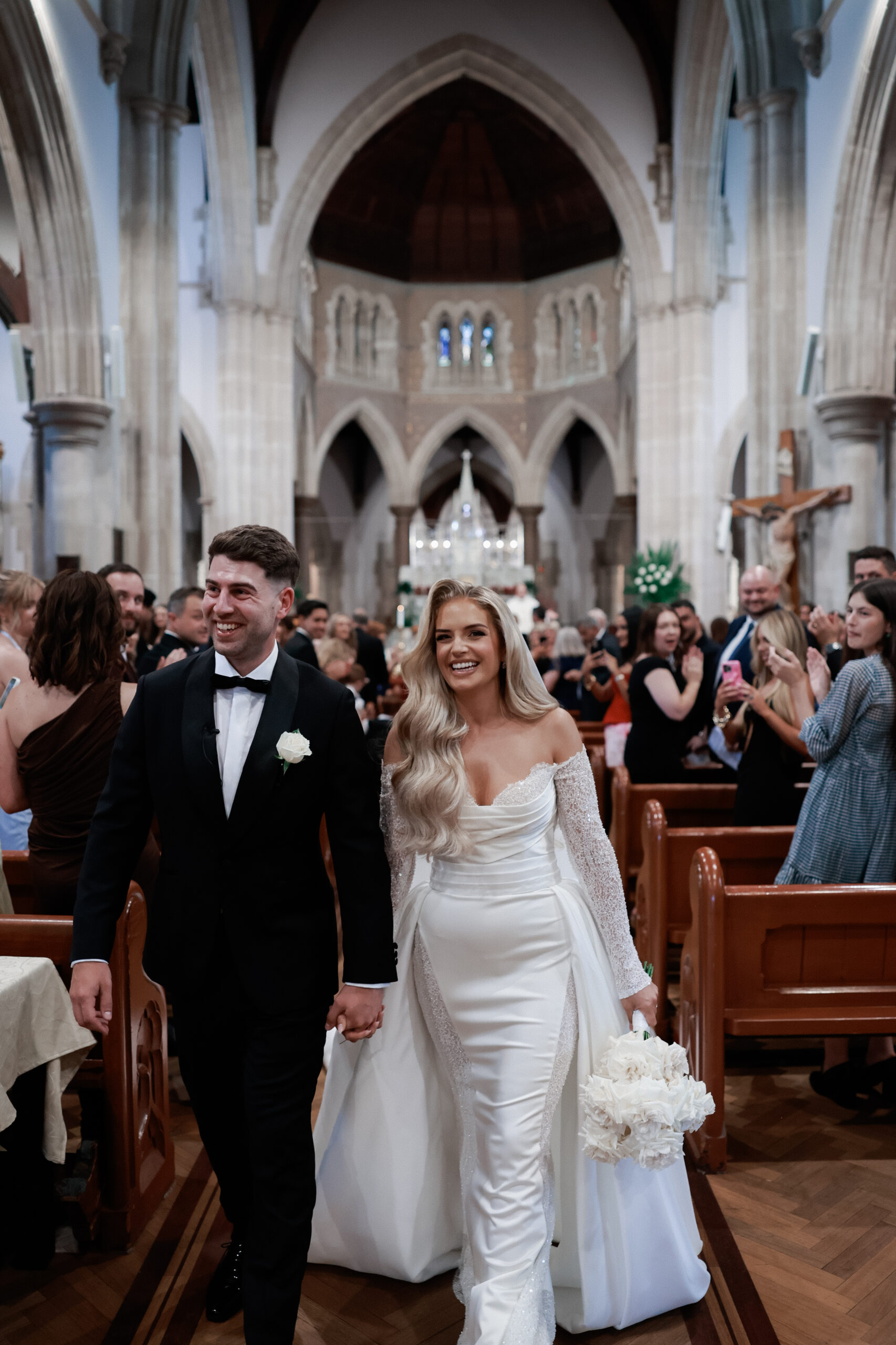 Bride and groom walking out of church with their guests surrounding them. 