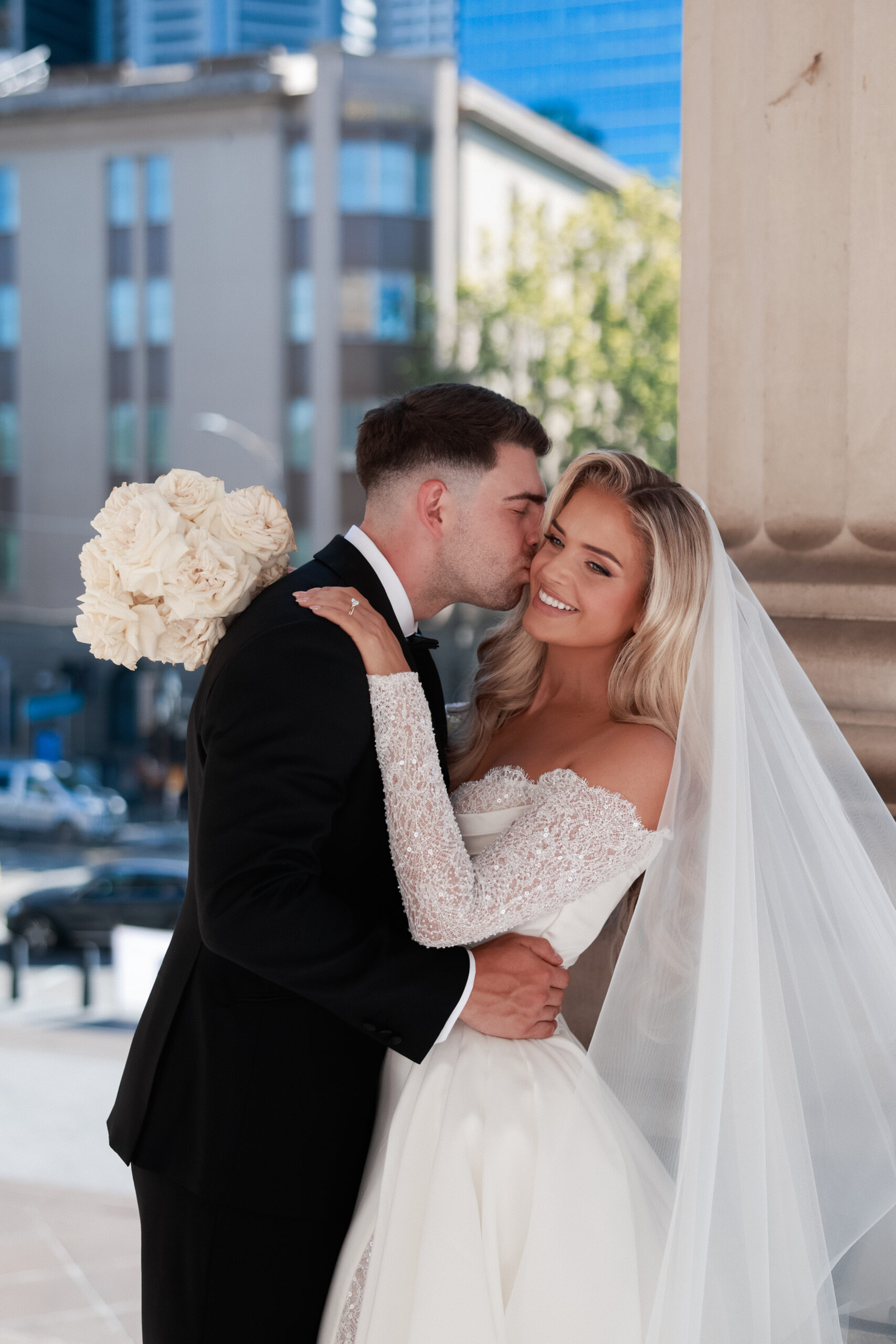 Bride and groom posing for wedding photo, groom kissing bride on the cheek.