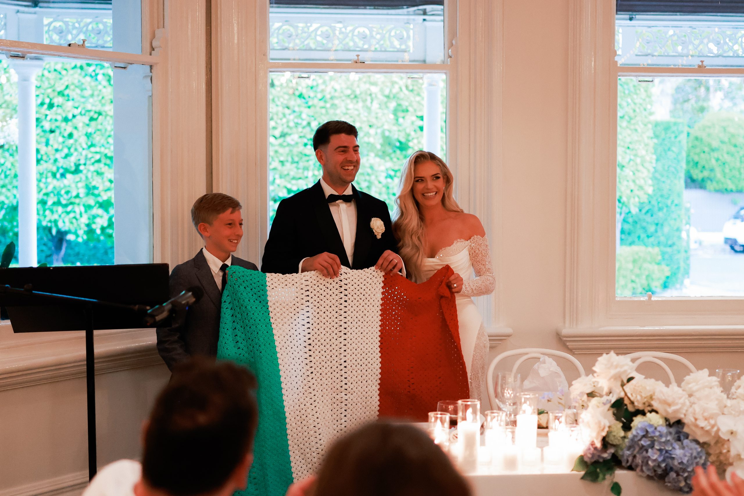 Bride. groom and little boy holding knitted italian flag style blanket. 