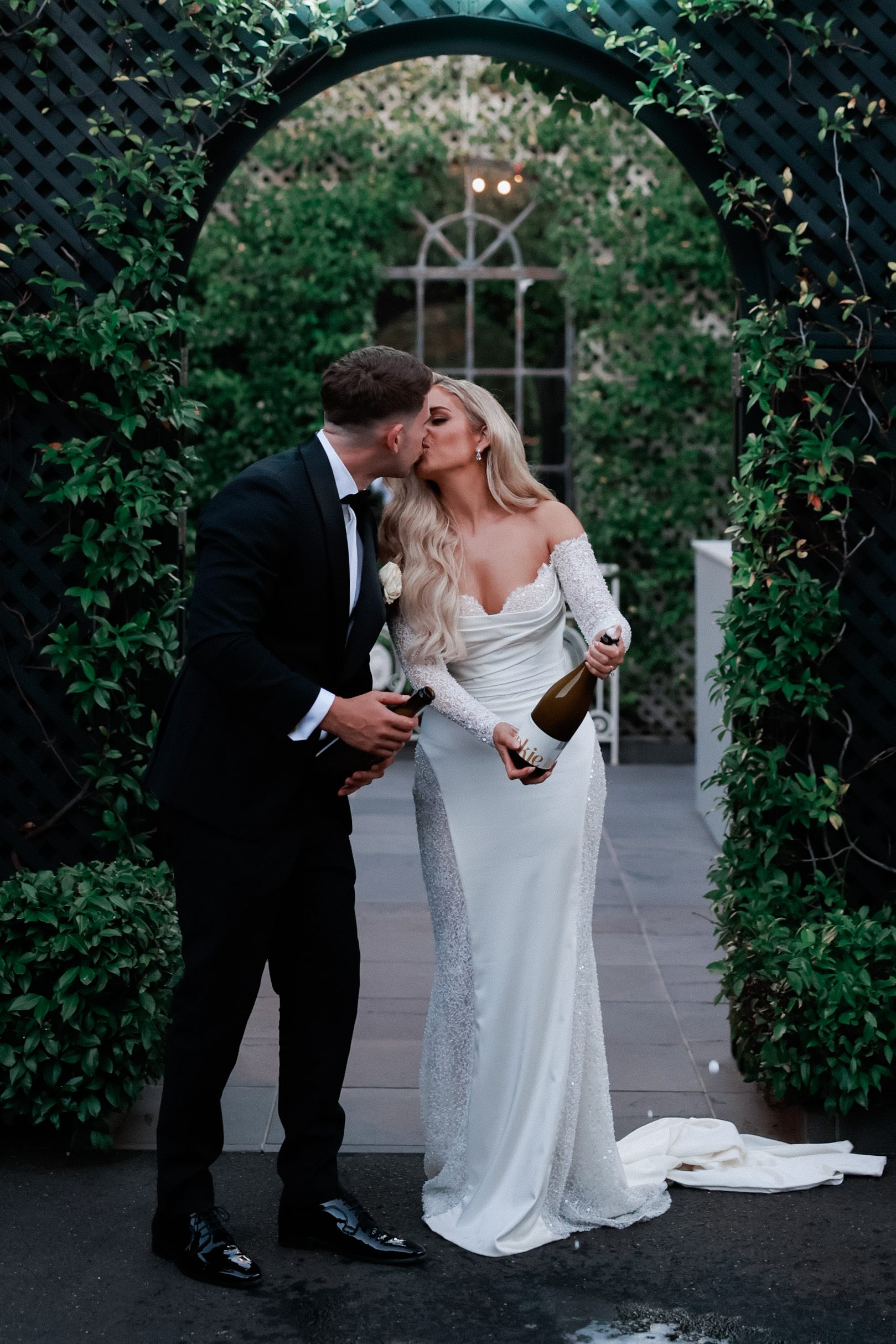 Bride and groom kissing while holding bottles of champagne