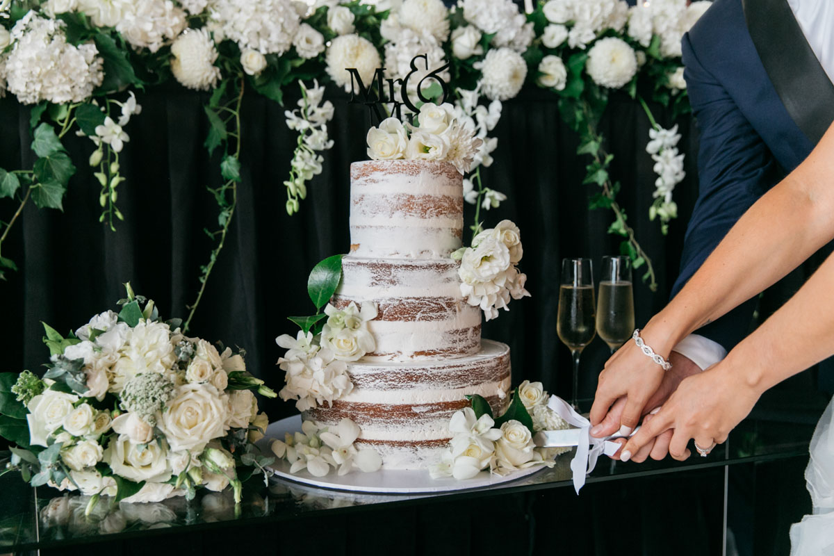 naked three tier wedding cake with white roses and greenery 